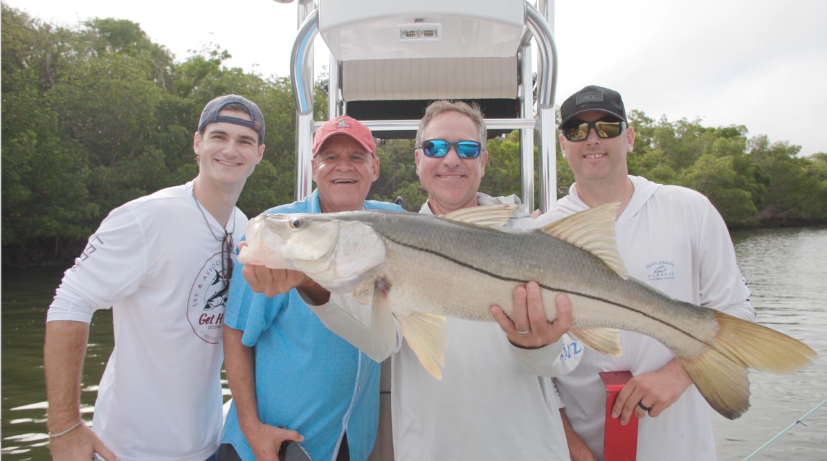 Four anglers holding a large snook on the boat